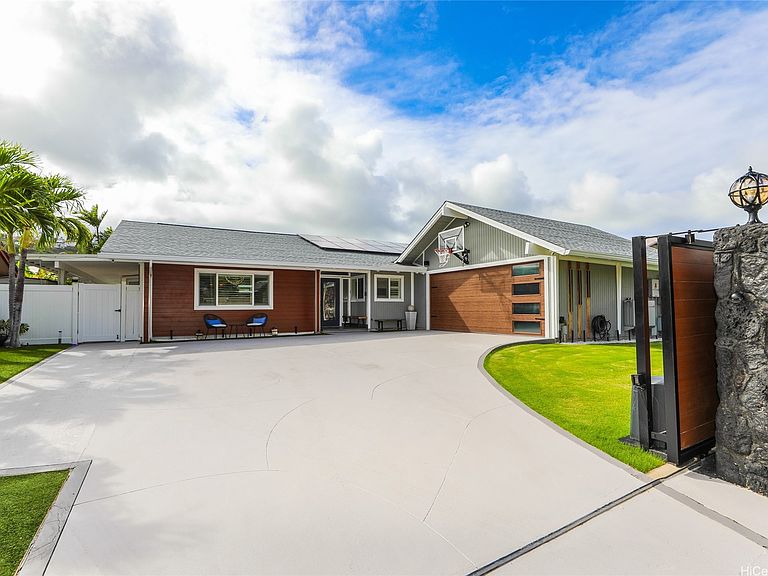 Front elevation of 654 Lunalilo Home Rd, a single-story Hawai'i Kai home with a low-pitch roof, wood-clad facade, and solar panels above a long concrete driveway