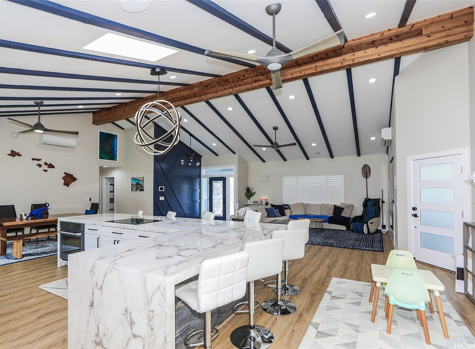 Tight crop of the kitchen island's marble waterfall edge at 654 Lunalilo Home Rd, with three white cushioned bar stools pulled up to it and wide-plank wood floor in the foreground